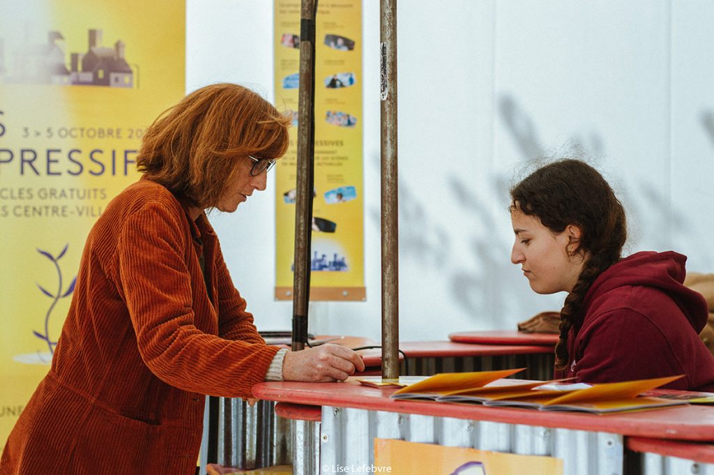 Une personne à l'accueil présente le programme du festival Les Expressifs.